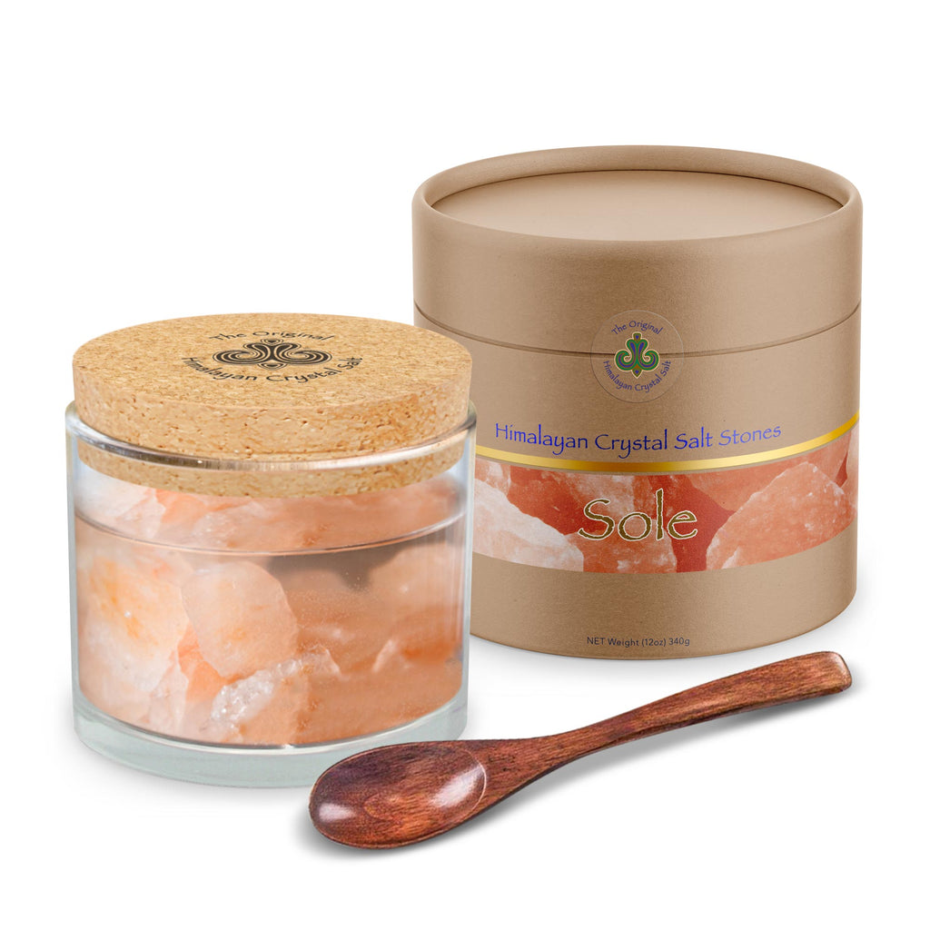 Sole Jar Plus Stones product glass jar filled with water and Himalayan Crystal Salt stones with cork cover and tan product box both featuring Himalayan Crystal Salt logo, and wooden spoon, on white background