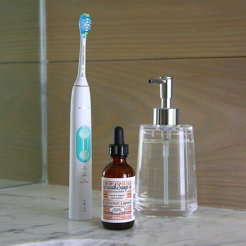 Cinnamon Tooth Soap white and turquoise standing electric toothbrush brown bottle with black dropper top with brown and white label, clear glass dispenser